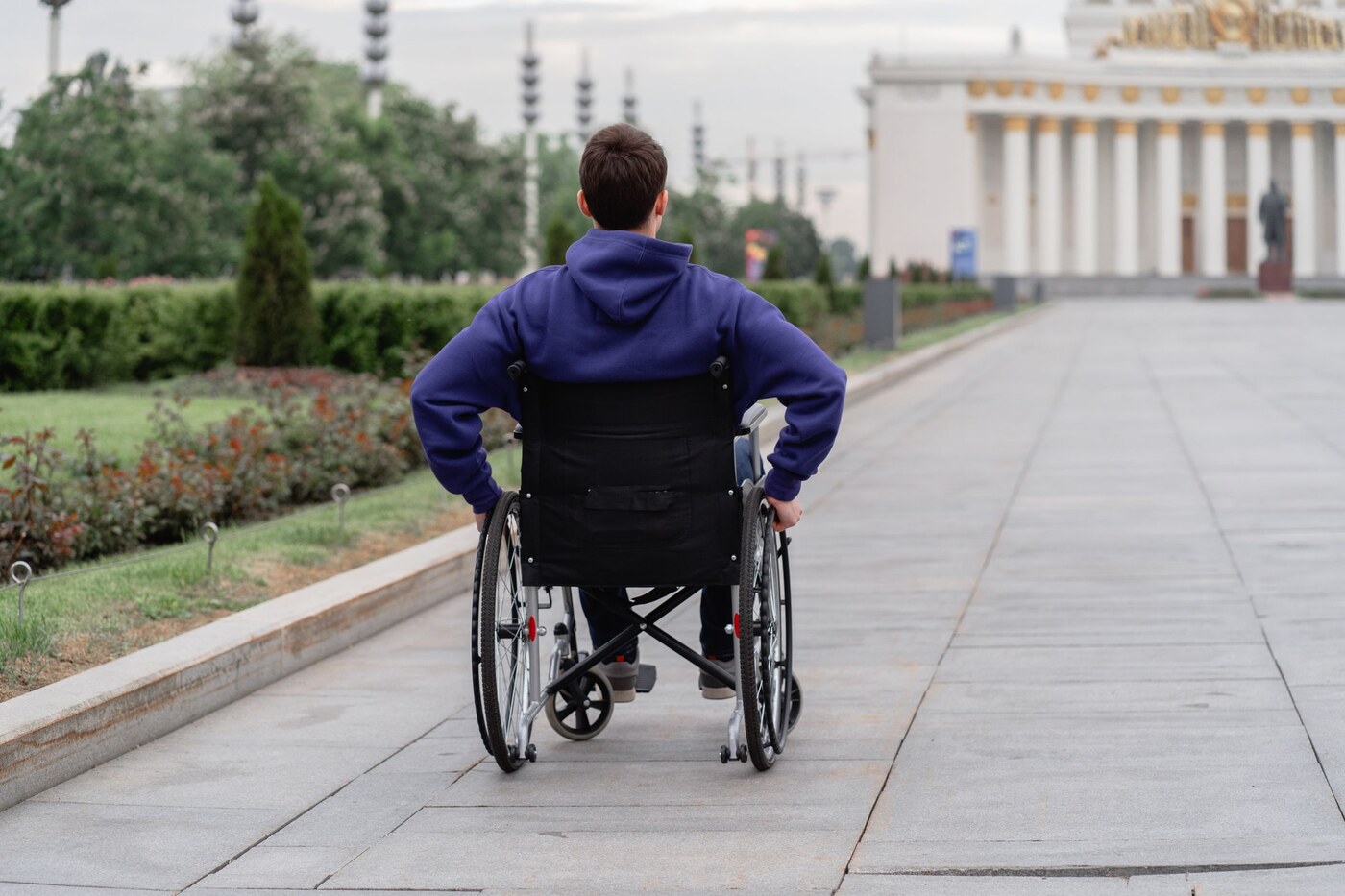 Un homme en fauteuil roulant vu de dos dans un espace extérieur